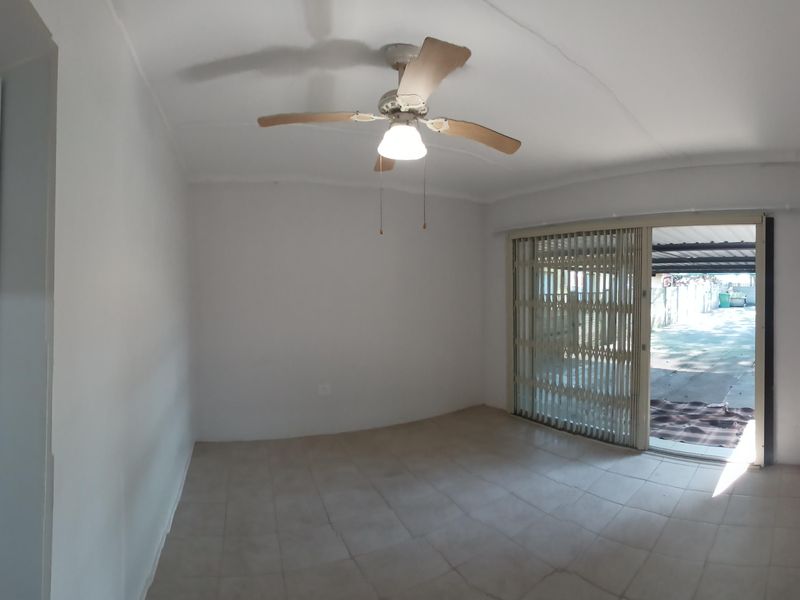 An empty living room featuring tiled flooring, a ceiling fan, and a sliding glass door with a security gate leading to the exterior.