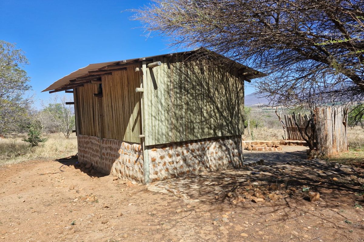 A rustic farm outbuilding featuring a stone masonry base, timber wall cladding, and a corrugated metal roof, set within a natural landscape.