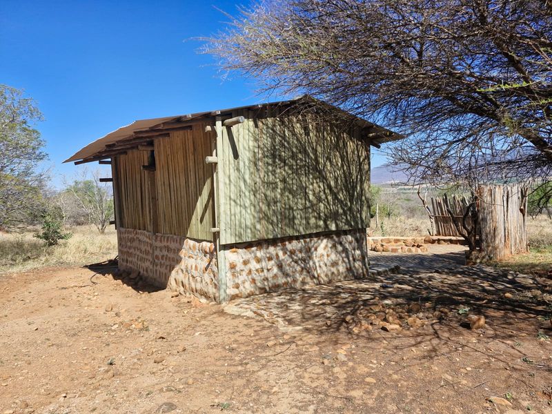 A rustic farm outbuilding featuring a stone masonry base, timber wall cladding, and a corrugated metal roof, set within a natural landscape.