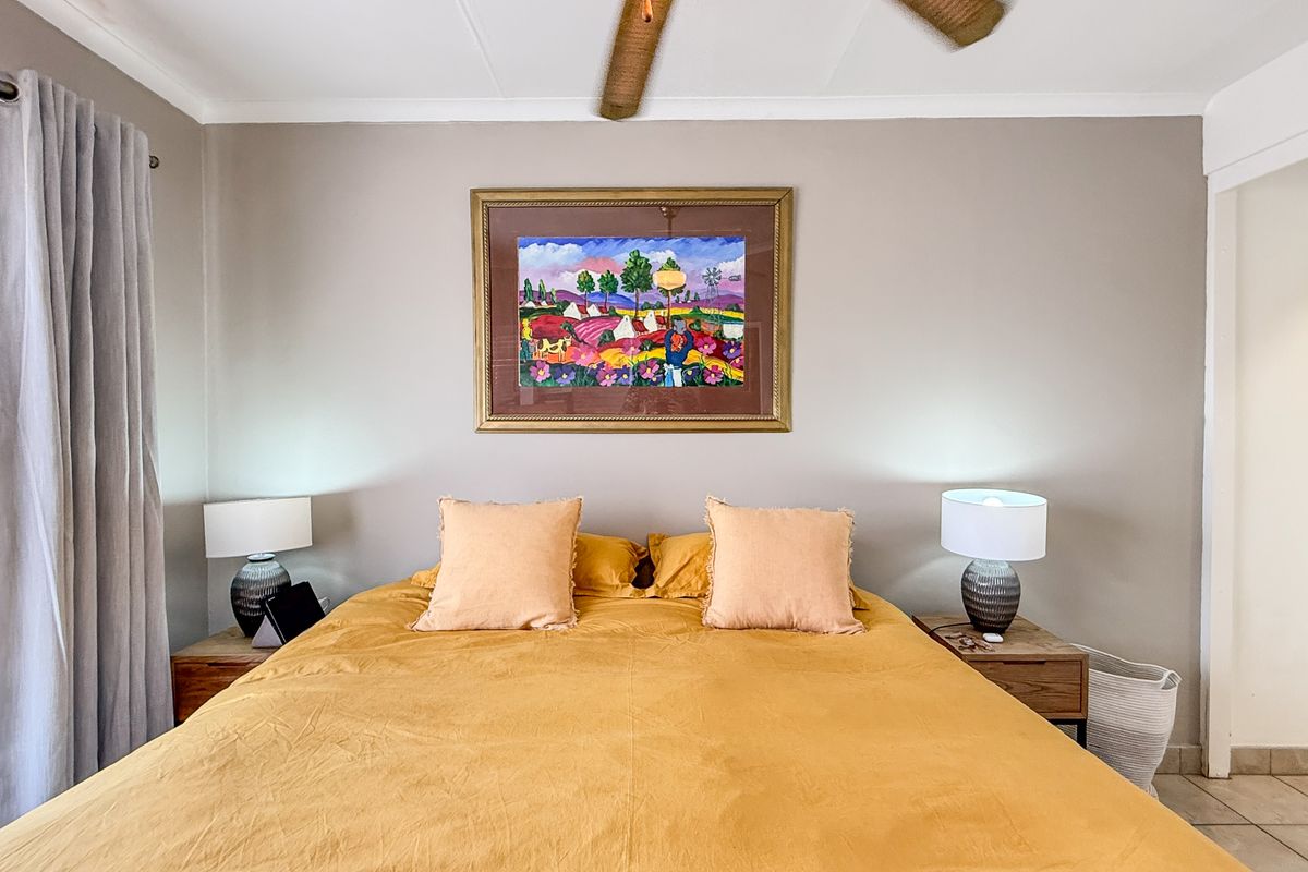 A well-maintained bedroom featuring a ceiling fan, tiled flooring, and large windows with curtains, providing a comfortable and functional living space.