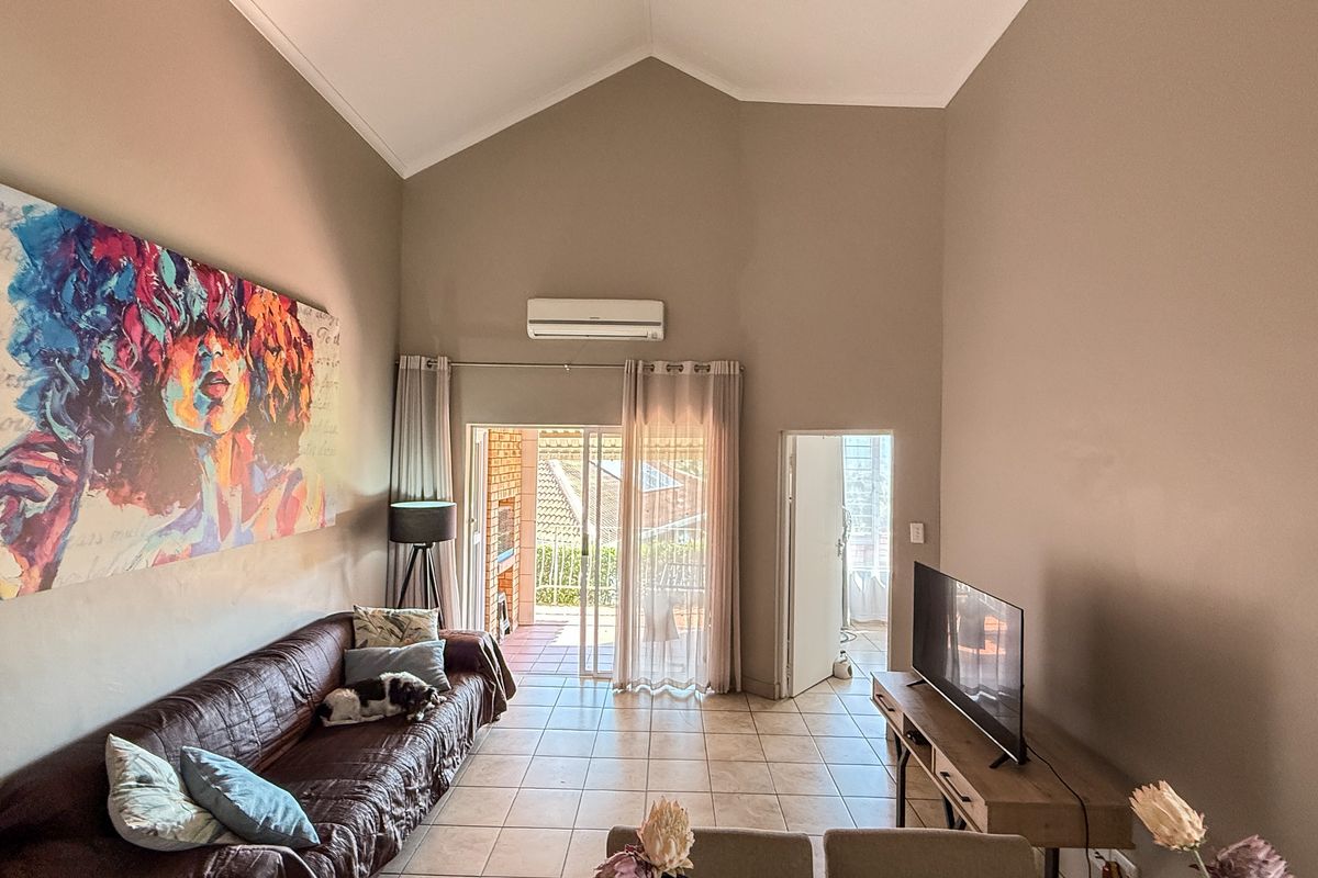 Spacious living room featuring high vaulted ceilings, tiled flooring, and direct access to a covered balcony through sliding glass doors.
