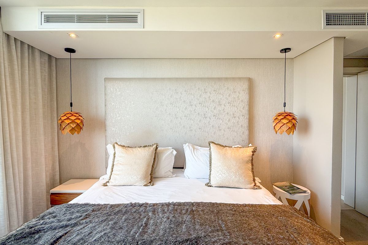 A modern bedroom featuring a built-in headboard, recessed ceiling lighting, and integrated air conditioning vents.