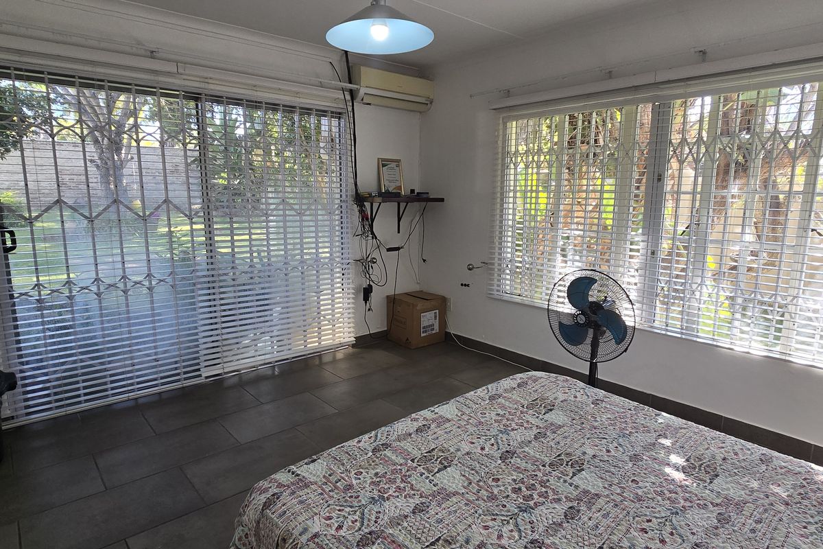 A bedroom featuring tiled flooring, large windows with security gates, and a wall-mounted air conditioning unit.