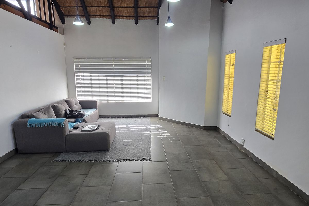 Spacious living area featuring high vaulted ceilings with exposed timber beams, large format floor tiles, and multiple windows fitted with venetian blinds.