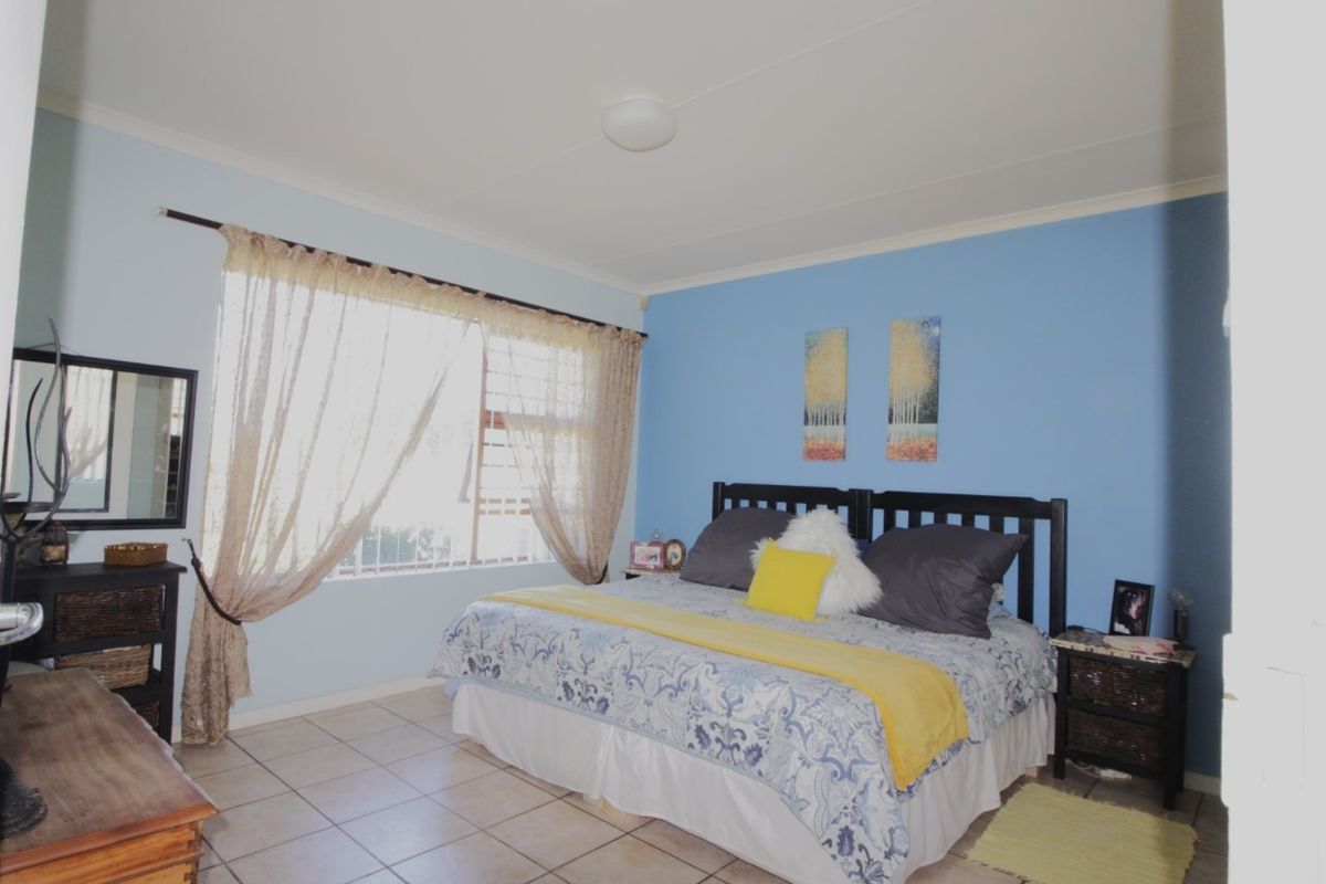 A spacious bedroom featuring tiled flooring, a large window with curtain rod, and a central ceiling light fixture.