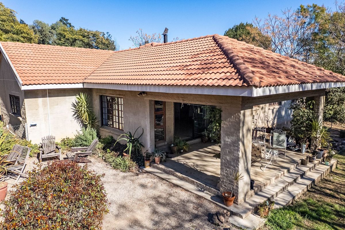 Rear view of a single-story house featuring a covered patio, tiled roof, and surrounding garden area with gravel ground cover.