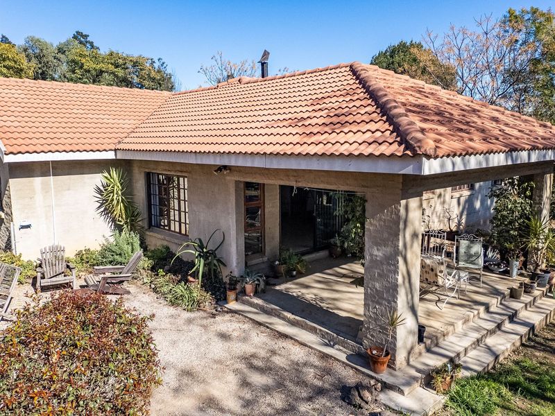 Rear view of a single-story house featuring a covered patio, tiled roof, and surrounding garden area with gravel ground cover.