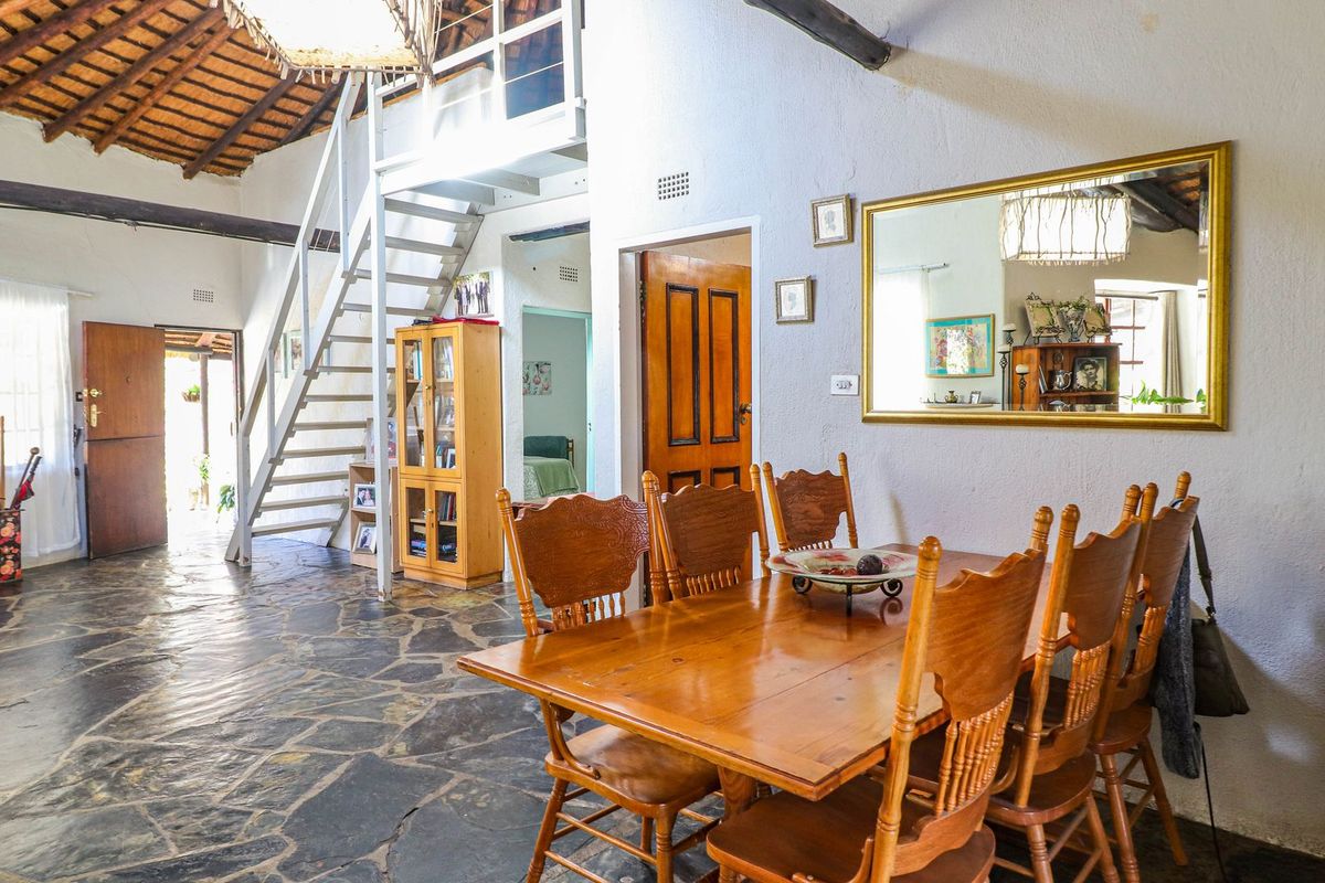 Spacious living area featuring rustic stone flooring, vaulted ceilings with exposed timber rafters, and a staircase leading to a mezzanine level.