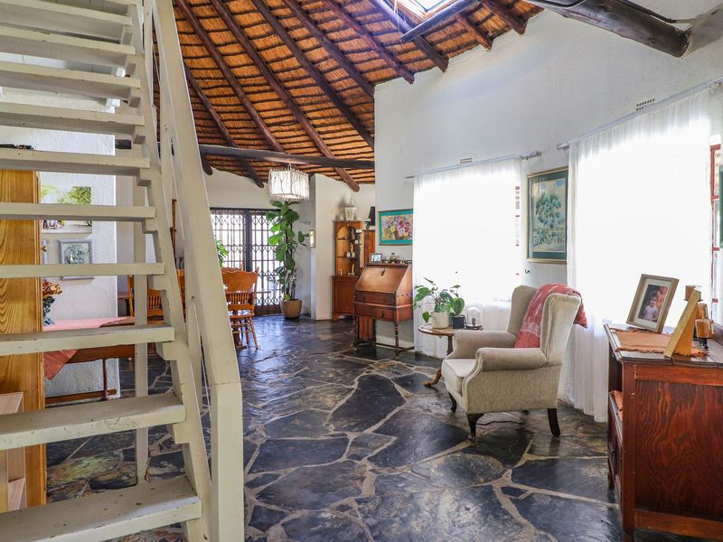 Spacious open-plan living area featuring unique exposed thatch roofing, a skylight, and rustic flagstone flooring with a central wooden staircase.