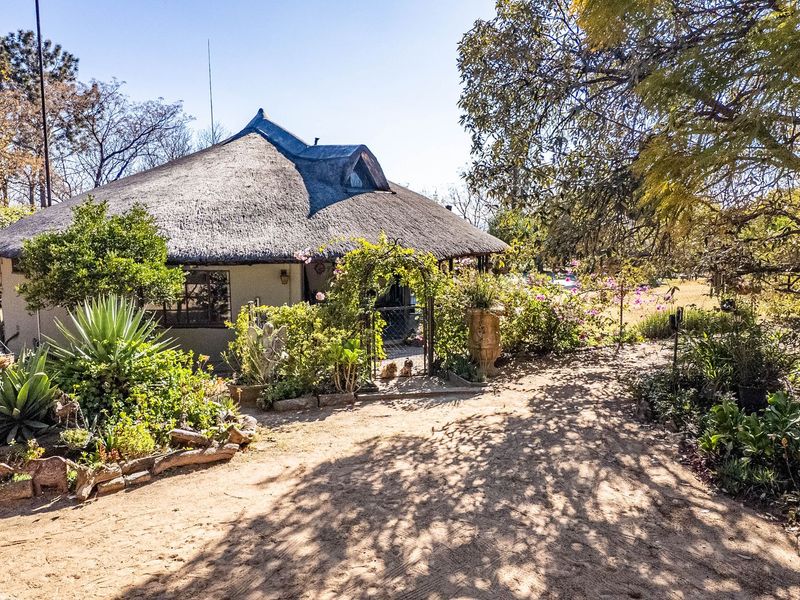 A rear view of a house featuring a traditional thatched roof, a dormer window, and a mature garden with a gated entrance.