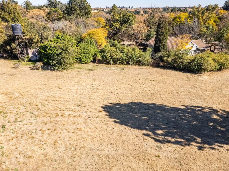 An aerial view of a large, open plot of land featuring mature trees, established vegetation, and a raised water tank structure.