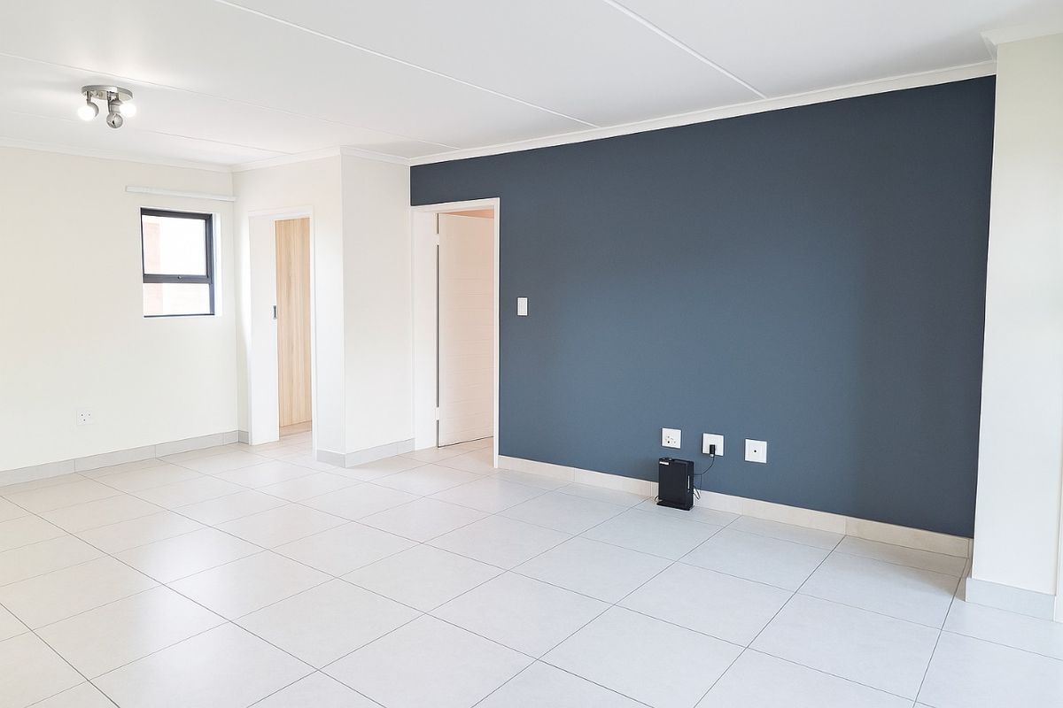 A bright and spacious living area featuring neutral tiled flooring, a modern dark blue feature wall, and clean white finishes throughout.