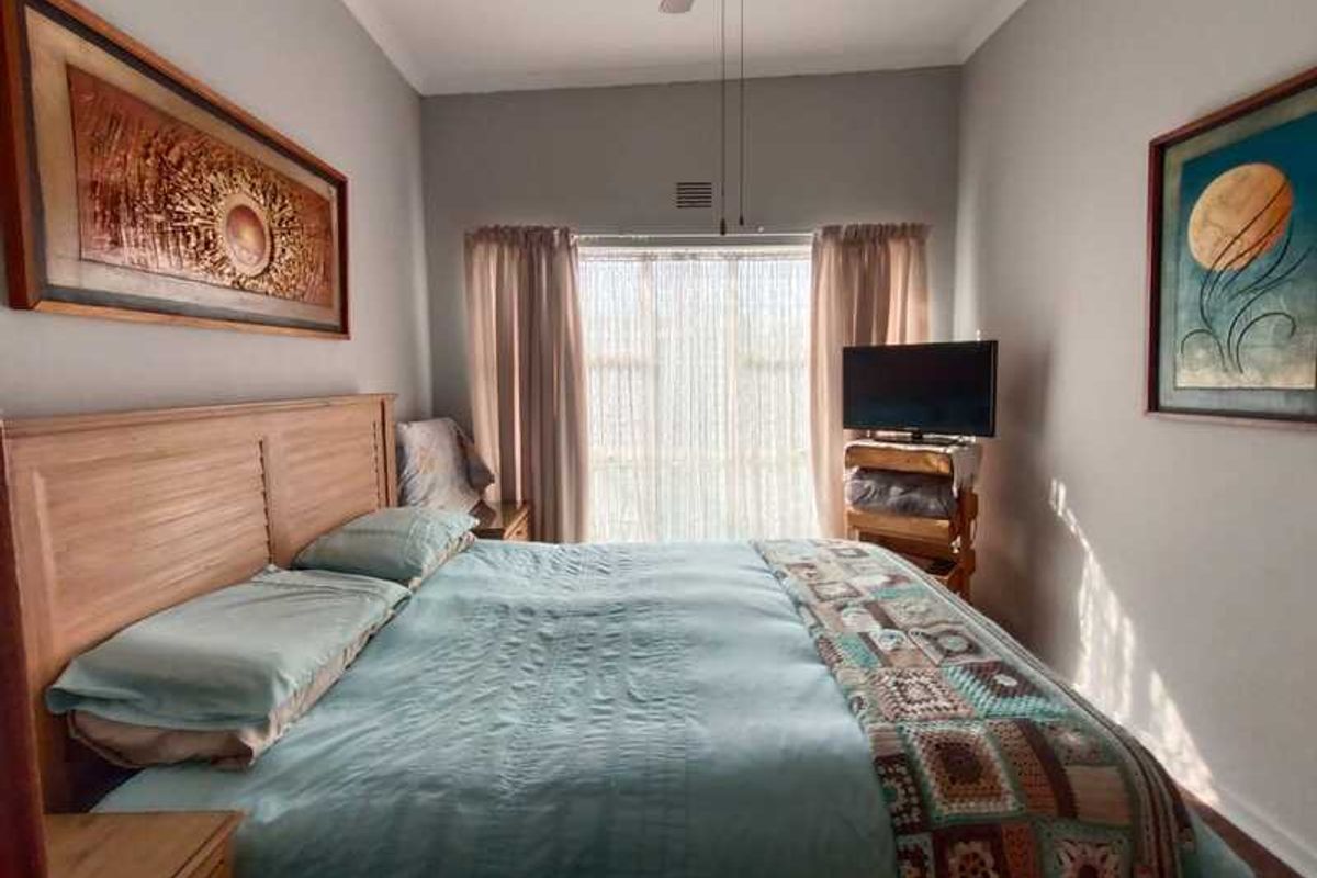 A well-lit bedroom featuring a high ceiling, ceiling fan, and large sliding glass doors providing natural light.