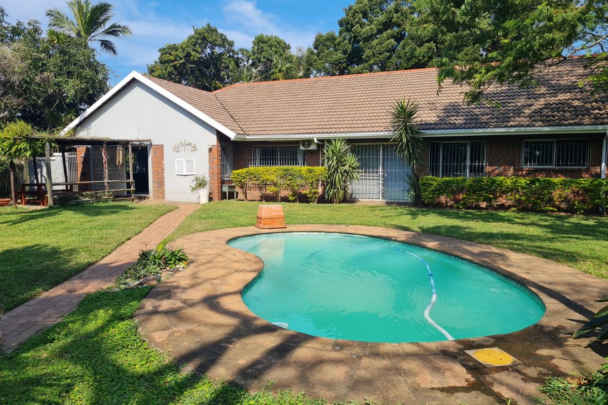 Rear view of the property featuring a swimming pool, landscaped garden, paved walkway, and a covered patio area attached to the main house.
