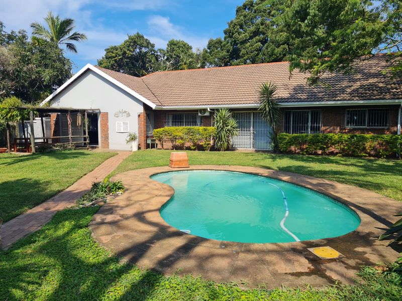 Rear view of the property featuring a swimming pool, landscaped garden, paved walkway, and a covered patio area attached to the main house.
