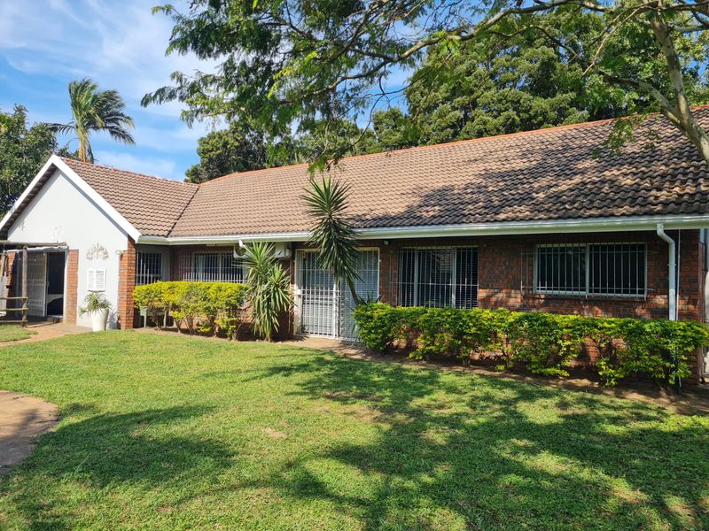 A single-story brick house featuring a tiled roof, security bars on windows, and a well-maintained front lawn with mature trees.