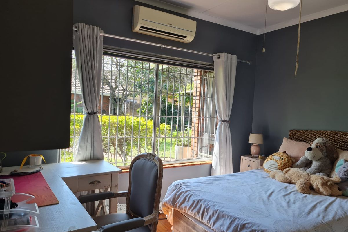 A bedroom featuring dark painted walls, a large window with security bars, and a wall-mounted air conditioning unit.