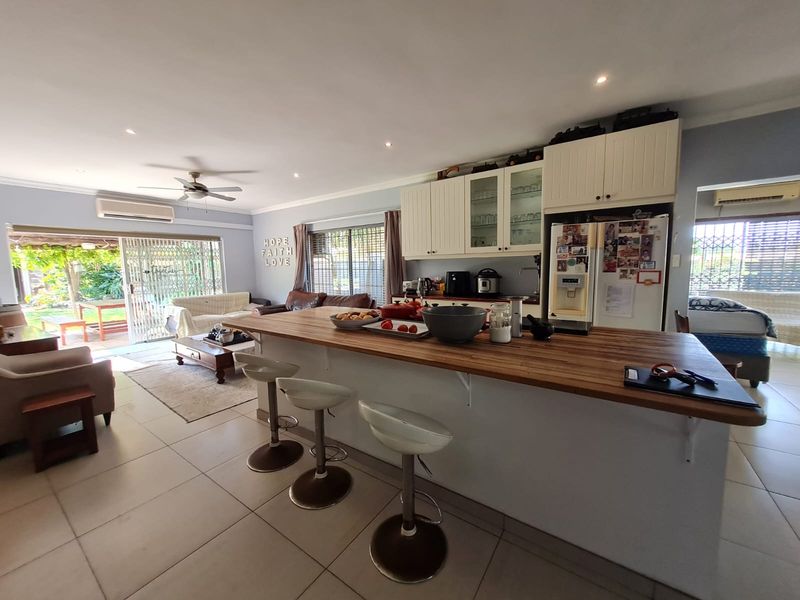 Open-plan kitchen and living area featuring a large wooden breakfast bar, tiled flooring, and direct access to the outdoor patio through sliding doors.
