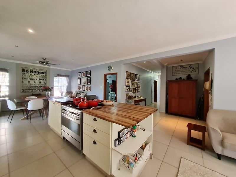 Open-plan kitchen and living area featuring a central island with a wooden countertop, built-in oven, and tiled flooring throughout.