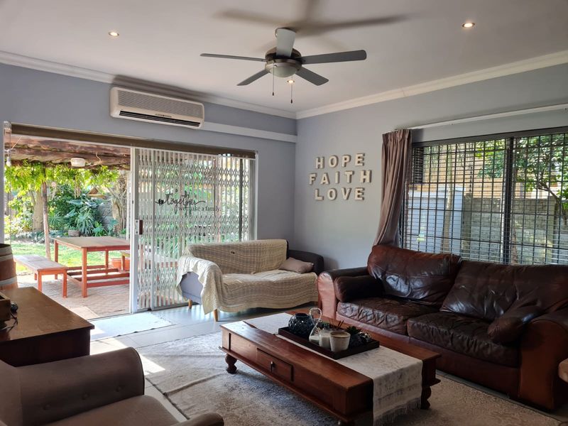 A comfortable living room featuring a ceiling fan, wall-mounted air conditioning unit, and large sliding glass doors providing direct access to the outdoor patio area.