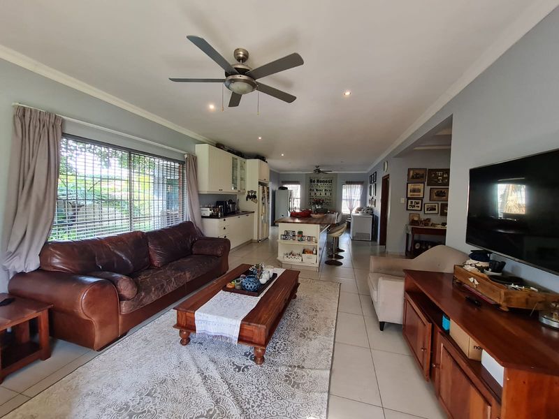 Open-plan living and kitchen area featuring tiled flooring, a central kitchen island, and a ceiling fan, creating a functional and connected living space.