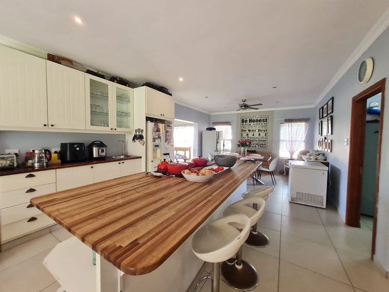 Spacious open-plan kitchen featuring a large wooden breakfast bar, white cabinetry, and tiled flooring, seamlessly flowing into the adjacent dining area.