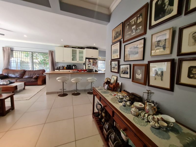 Open-plan living area featuring a kitchen with a breakfast bar, tiled flooring, and recessed ceiling details, seamlessly connecting to the lounge space.