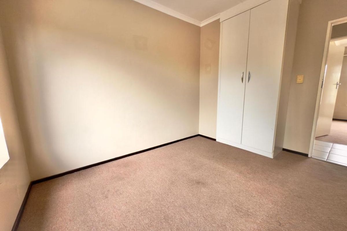 A neutral-toned bedroom featuring built-in cupboards and carpeted flooring, offering a clean and functional space ready for personalization.
