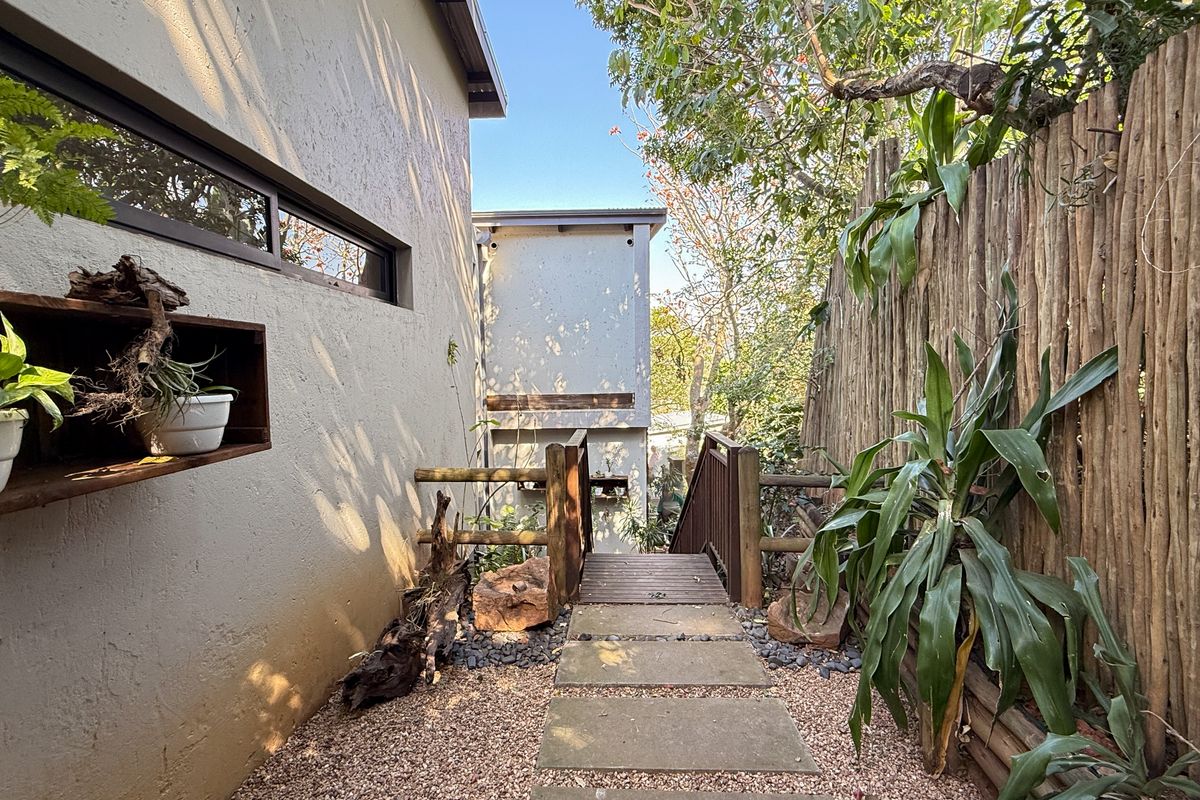 A landscaped side pathway featuring stone pavers, a wooden bridge, and a rustic timber fence, leading towards the rear of the townhouse property.