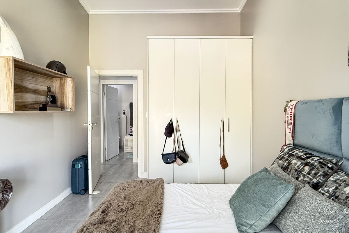 A well-maintained bedroom featuring built-in wardrobes, neutral wall tones, and tiled flooring, with an adjoining doorway leading to an en-suite bathroom.