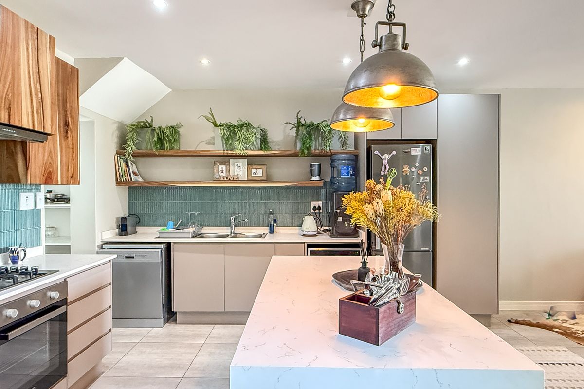 Modern kitchen featuring a central island with stone countertop, integrated cabinetry, tiled backsplash, built-in oven, gas hob, and industrial-style pendant lighting.
