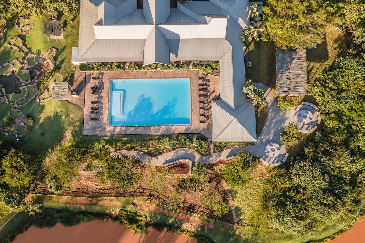 Aerial view of the property featuring a large swimming pool, paved patio area, landscaped gardens, and a scenic waterfront setting.