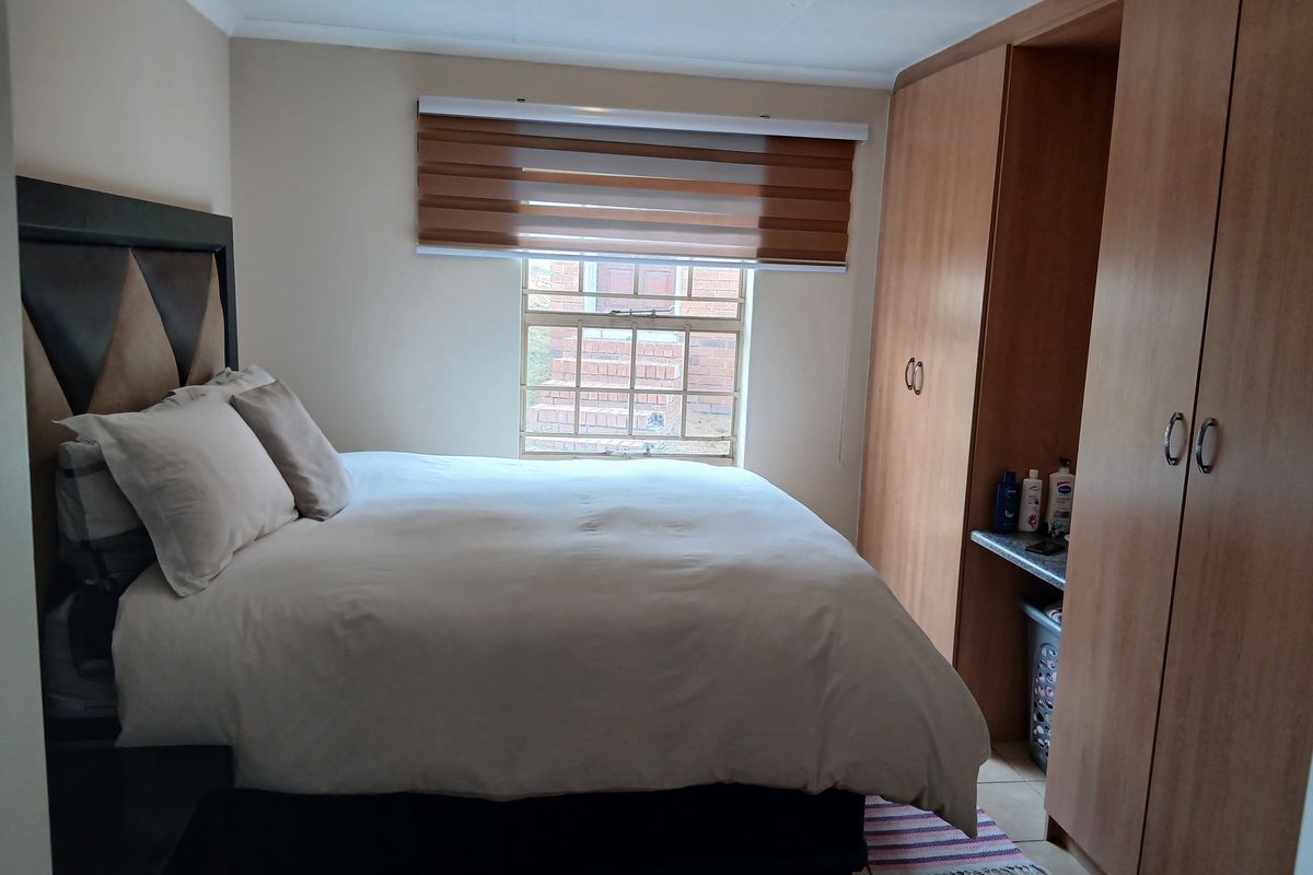 A functional bedroom featuring built-in wooden cabinetry and a window with fitted blinds, providing a practical and comfortable living space.
