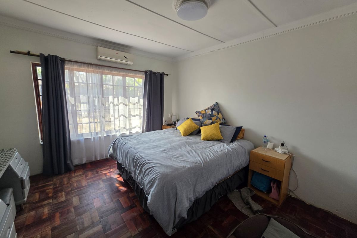 A bedroom featuring parquet flooring, a wall-mounted air conditioning unit, and a large window with natural light.