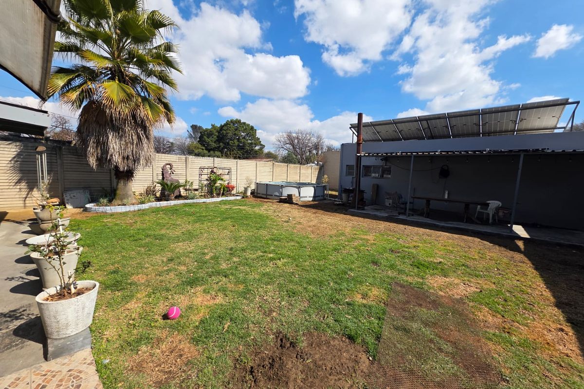 A spacious rear garden featuring a lawn area, a covered patio space, and solar panels installed on the roof of the adjacent structure.