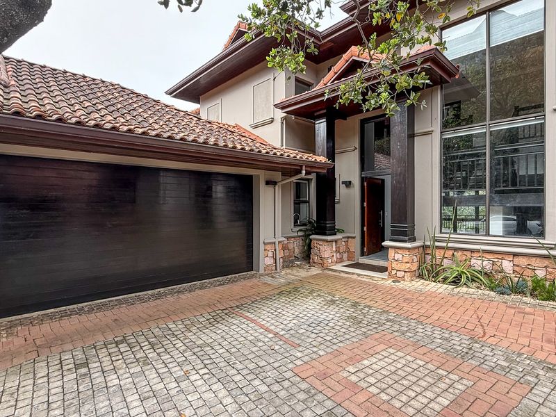 Front elevation of a townhouse featuring a double garage, paved driveway, stone cladding accents, and a prominent covered entrance with large glass windows.
