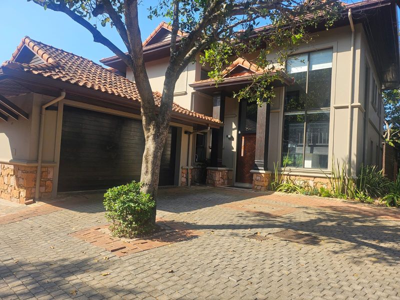 Front elevation of a double-storey townhouse featuring a paved driveway, double garage, stone cladding accents, and a prominent timber entrance door.