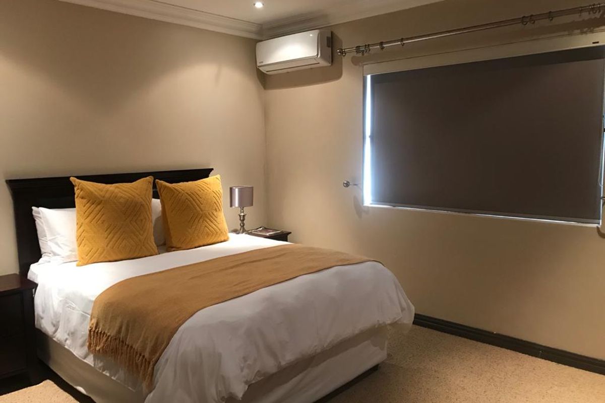 A well-maintained bedroom featuring neutral wall tones, carpeted flooring, a wall-mounted split-system air conditioner, and a roller blind for privacy.