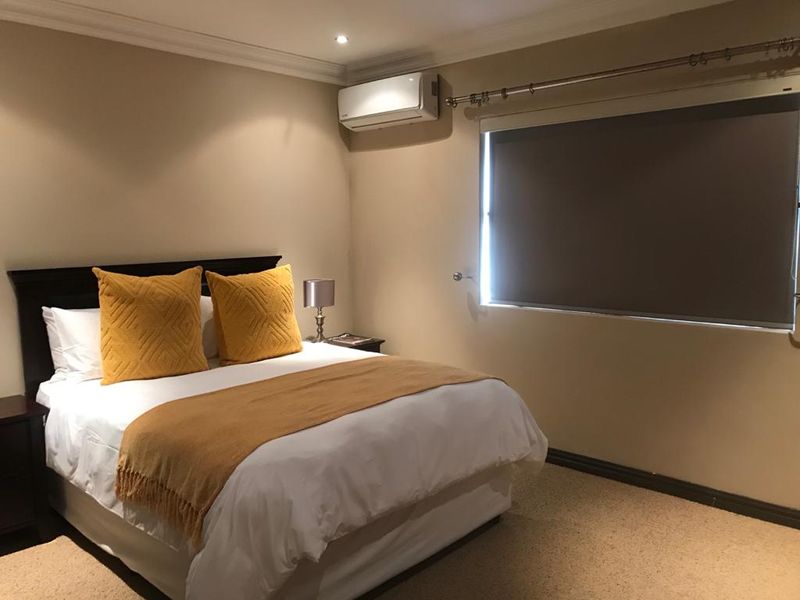 A well-maintained bedroom featuring neutral wall tones, carpeted flooring, a wall-mounted split-system air conditioner, and a roller blind for privacy.