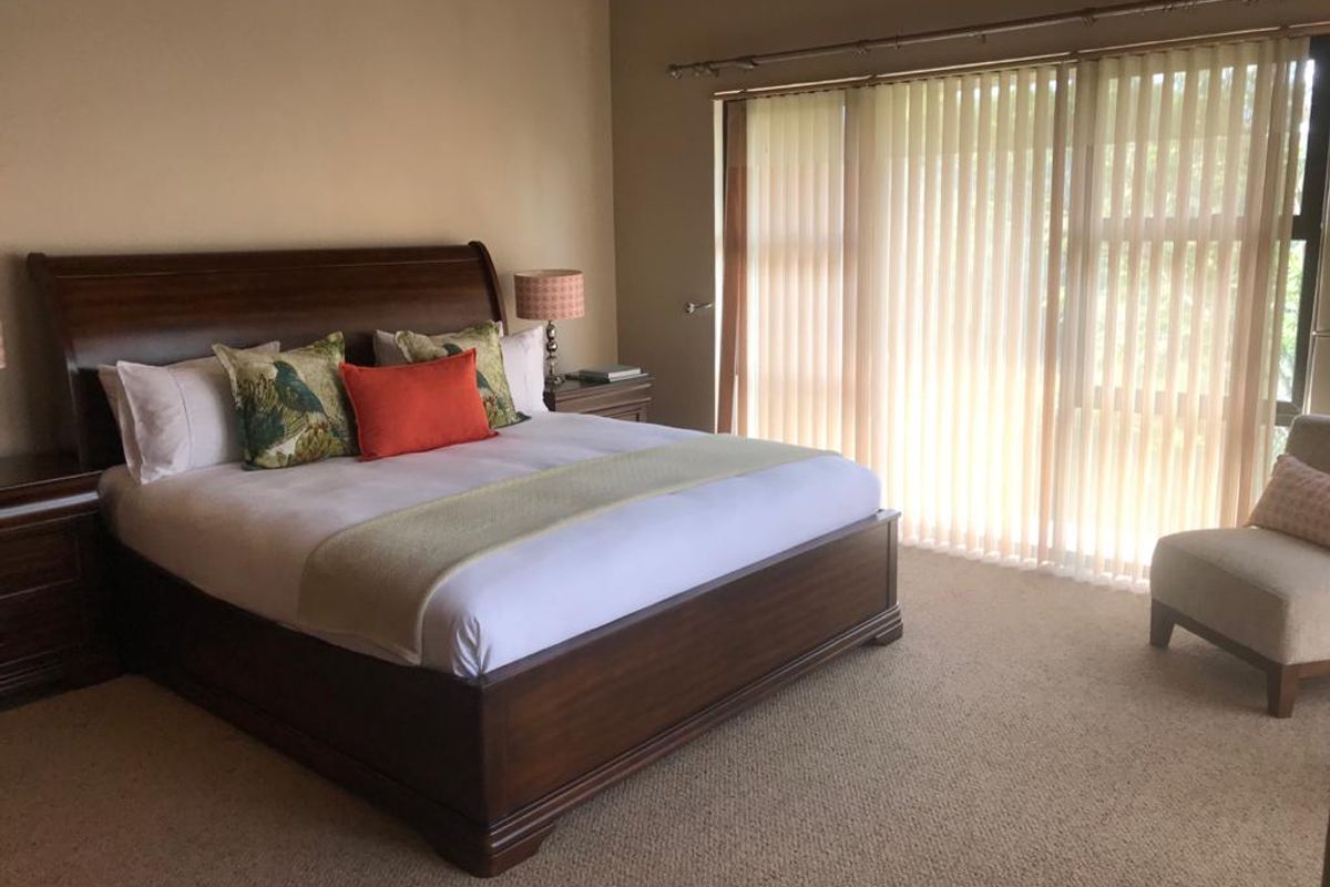 Spacious bedroom featuring neutral wall tones, carpeted flooring, and large sliding glass doors with vertical blinds providing natural light.