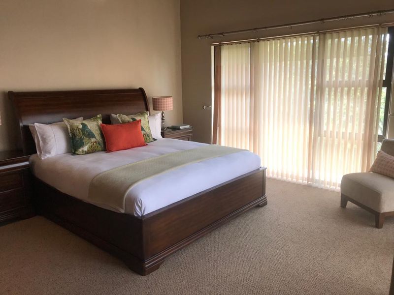 Spacious bedroom featuring neutral wall tones, carpeted flooring, and large sliding glass doors with vertical blinds providing natural light.