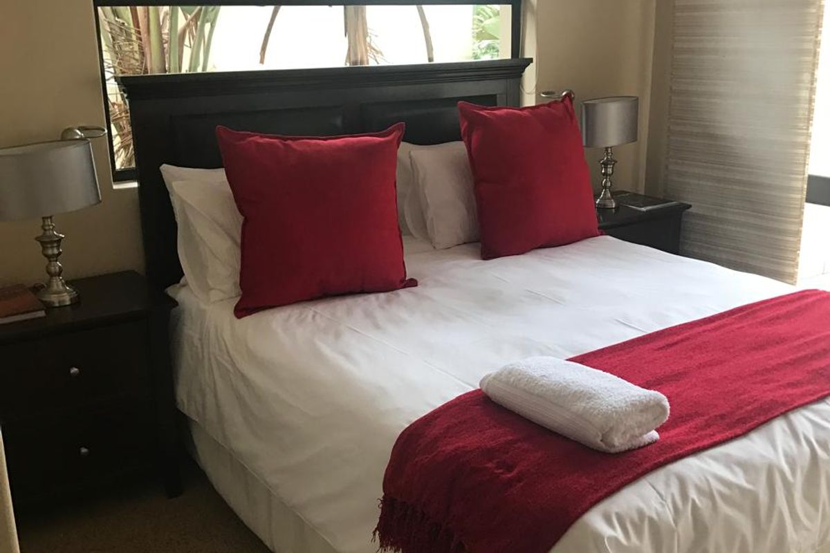 A cozy bedroom featuring carpeted flooring and a large window with an aluminium frame, providing natural light and a view of the garden.