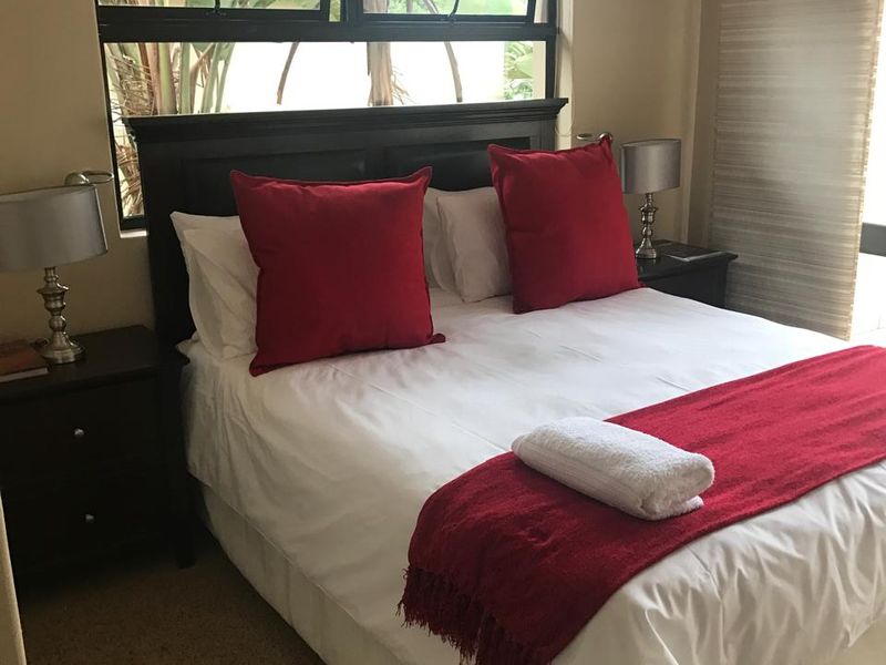 A cozy bedroom featuring carpeted flooring and a large window with an aluminium frame, providing natural light and a view of the garden.