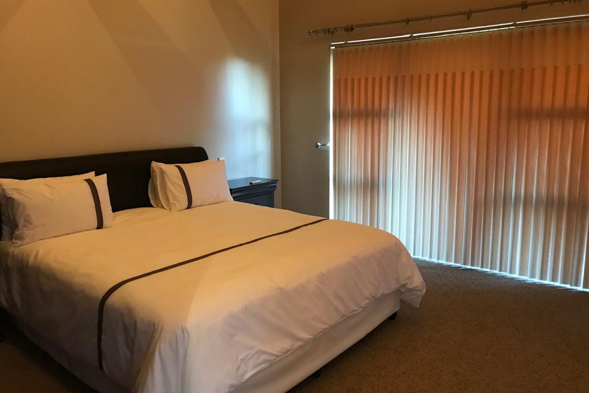 A spacious bedroom featuring neutral wall tones, carpeted flooring, and large vertical blinds covering the window area.
