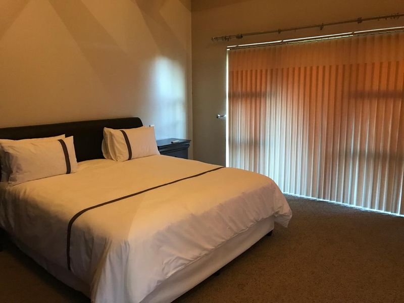 A spacious bedroom featuring neutral wall tones, carpeted flooring, and large vertical blinds covering the window area.