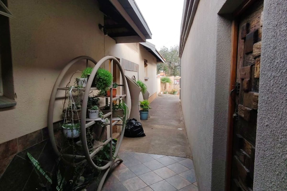 A narrow exterior side passage featuring tiled flooring and access to a textured wooden door, leading towards the rear of the property.