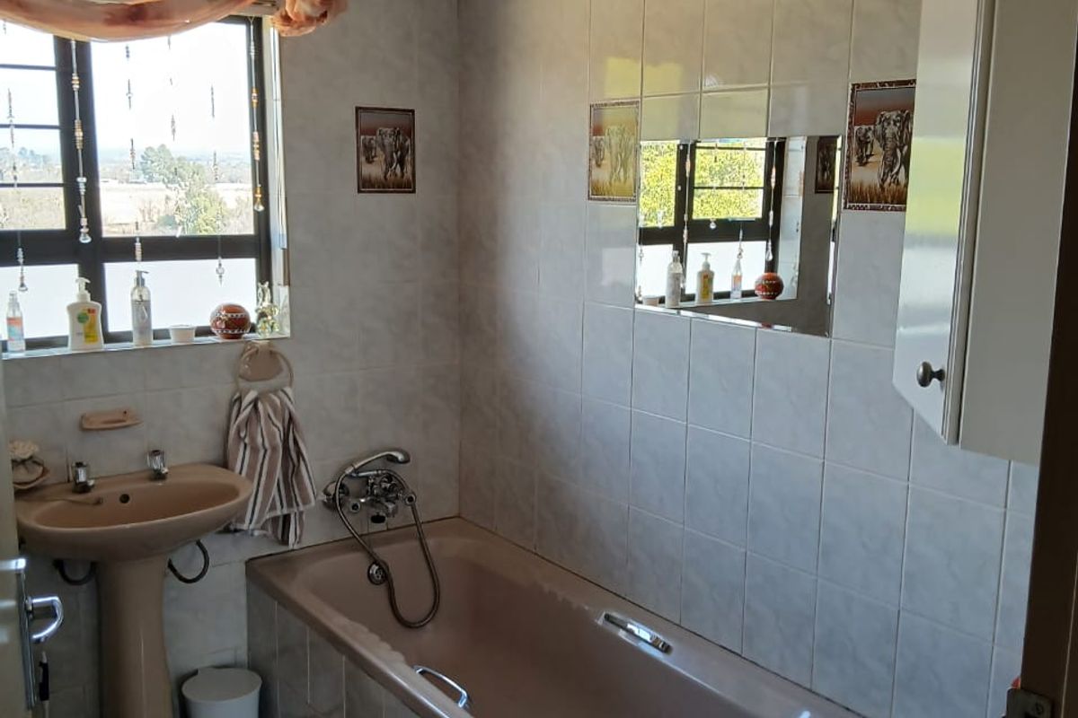 A functional bathroom featuring a built-in bathtub, pedestal basin, and tiled walls, offering a classic layout with natural light from the window.