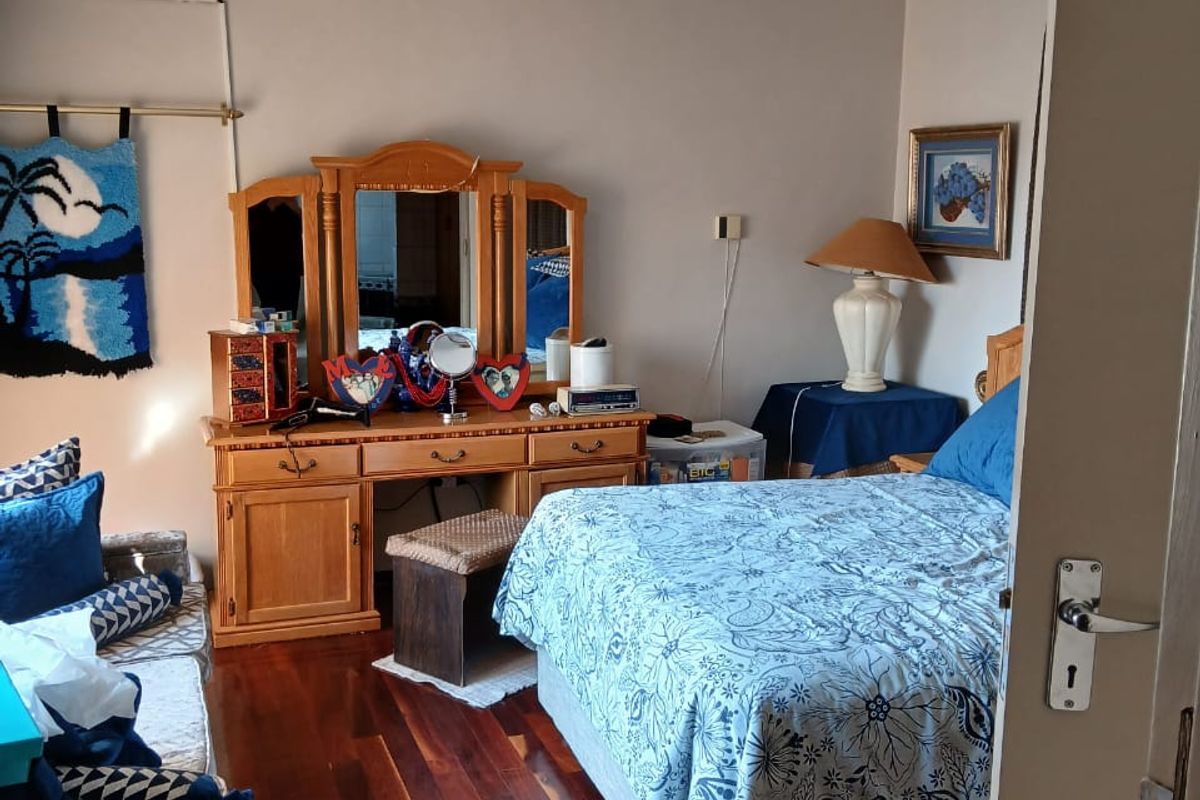 A well-maintained bedroom featuring polished hardwood flooring, a ceiling fan, and a wall-mounted air conditioning unit.