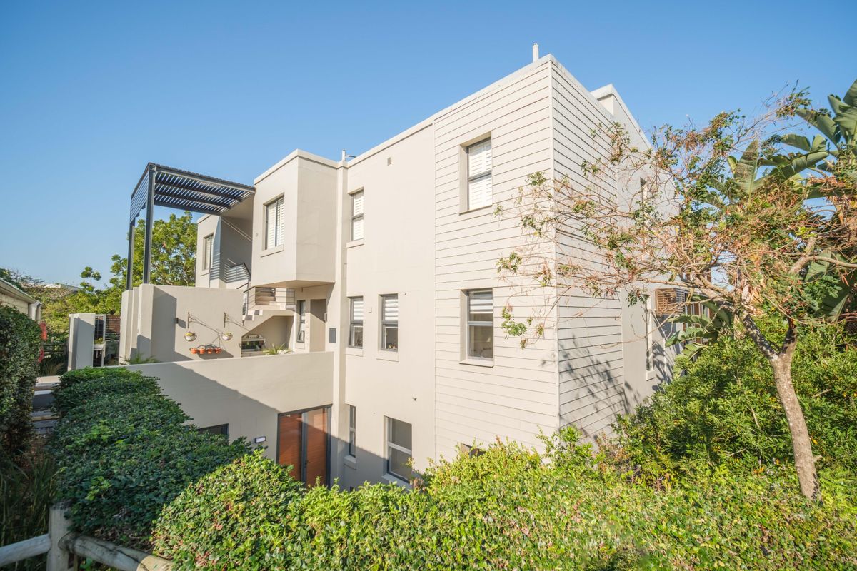 A view of the modern apartment building exterior, featuring clean lines, neutral cladding, and a private balcony area with a pergola.