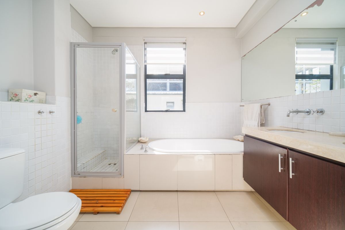 A functional bathroom featuring a built-in bathtub, separate glass-enclosed shower, wall-mounted vanity with stone countertop, and tiled flooring.